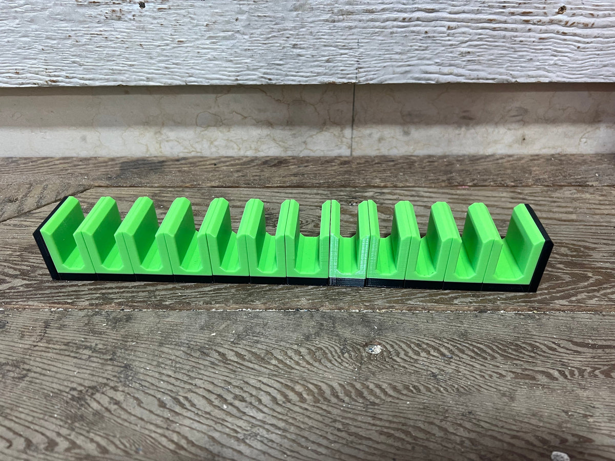 Empty row of bright green pliers holders with black end pieces on a wood surface.