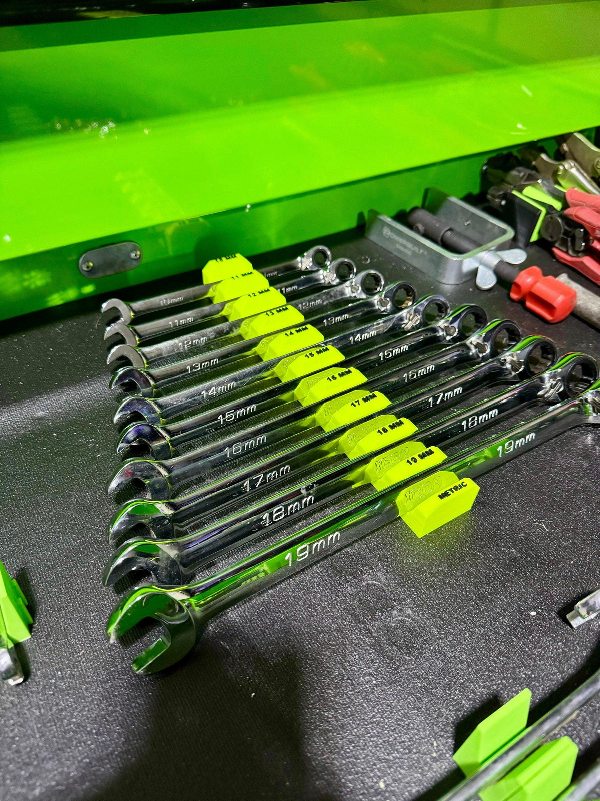 Angled view of a wrench set supported along the middle by a neon yellow size-labeled holder.