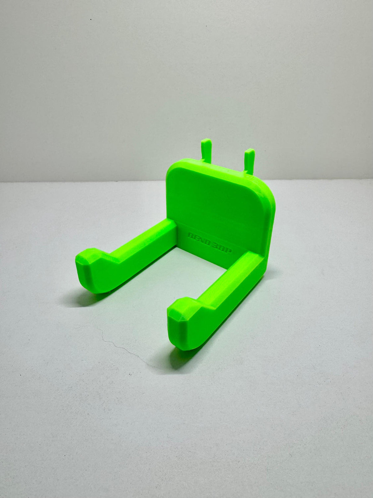 Bright green hammer holder with two projecting arms, raised tips and rear mounting tabs.