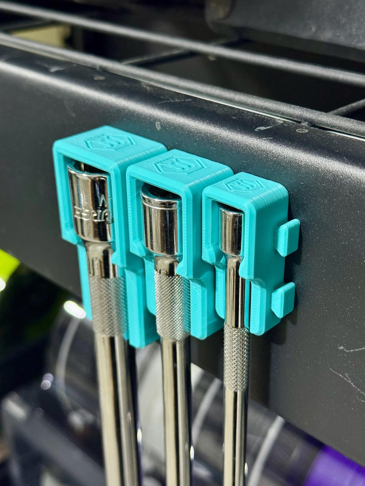 Teal holders gripping three extension heads along the side of a dark tool cart, viewed from above.