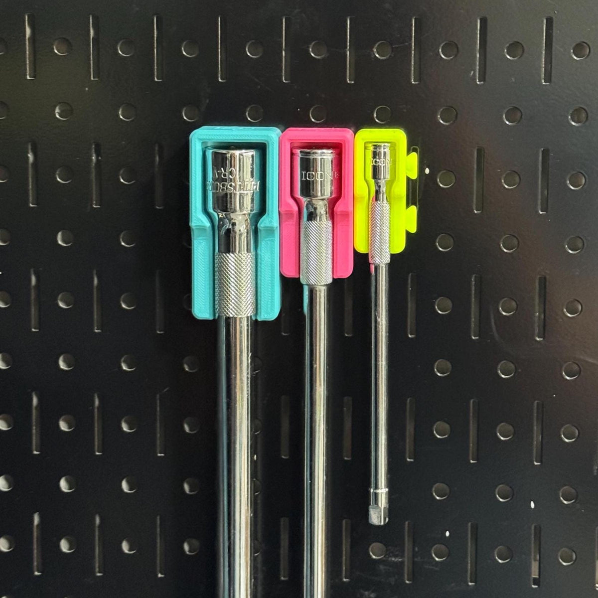 Front view of three socket extensions hanging at different lengths from teal, pink and yellow holders.
