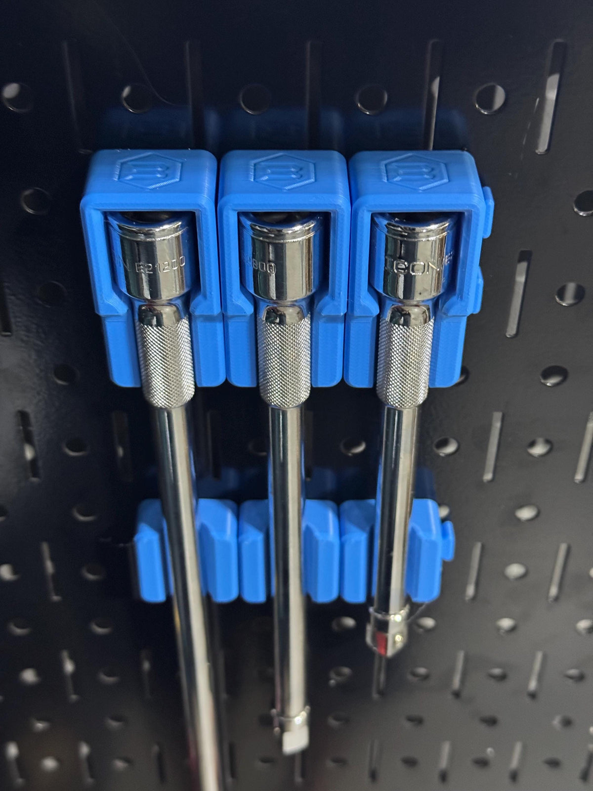 Three extension bars secured on black pegboard by blue head holders and separate blue lower supports.