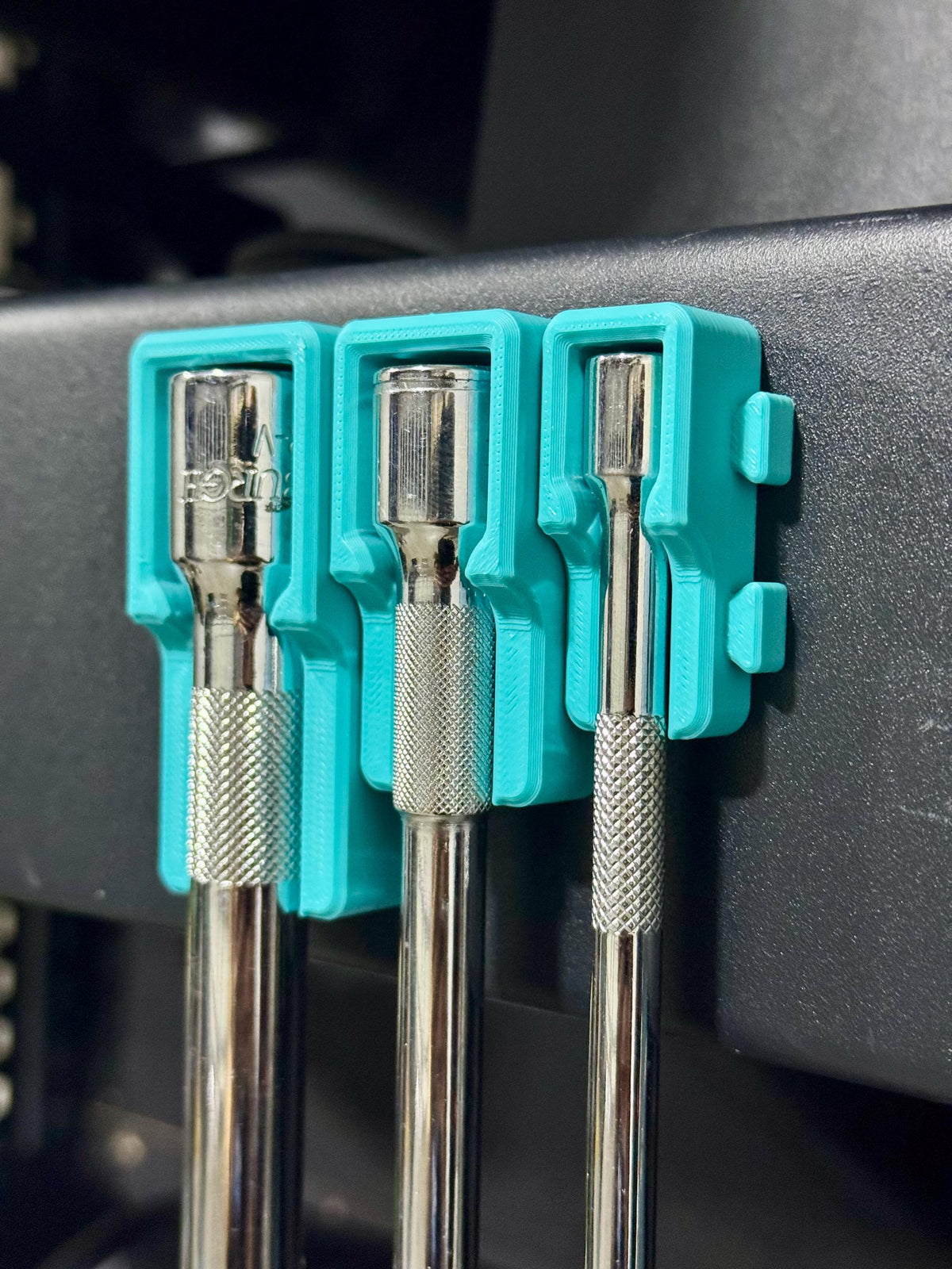 Close-up of three extension heads in linked teal holders along the side of a tool cart.