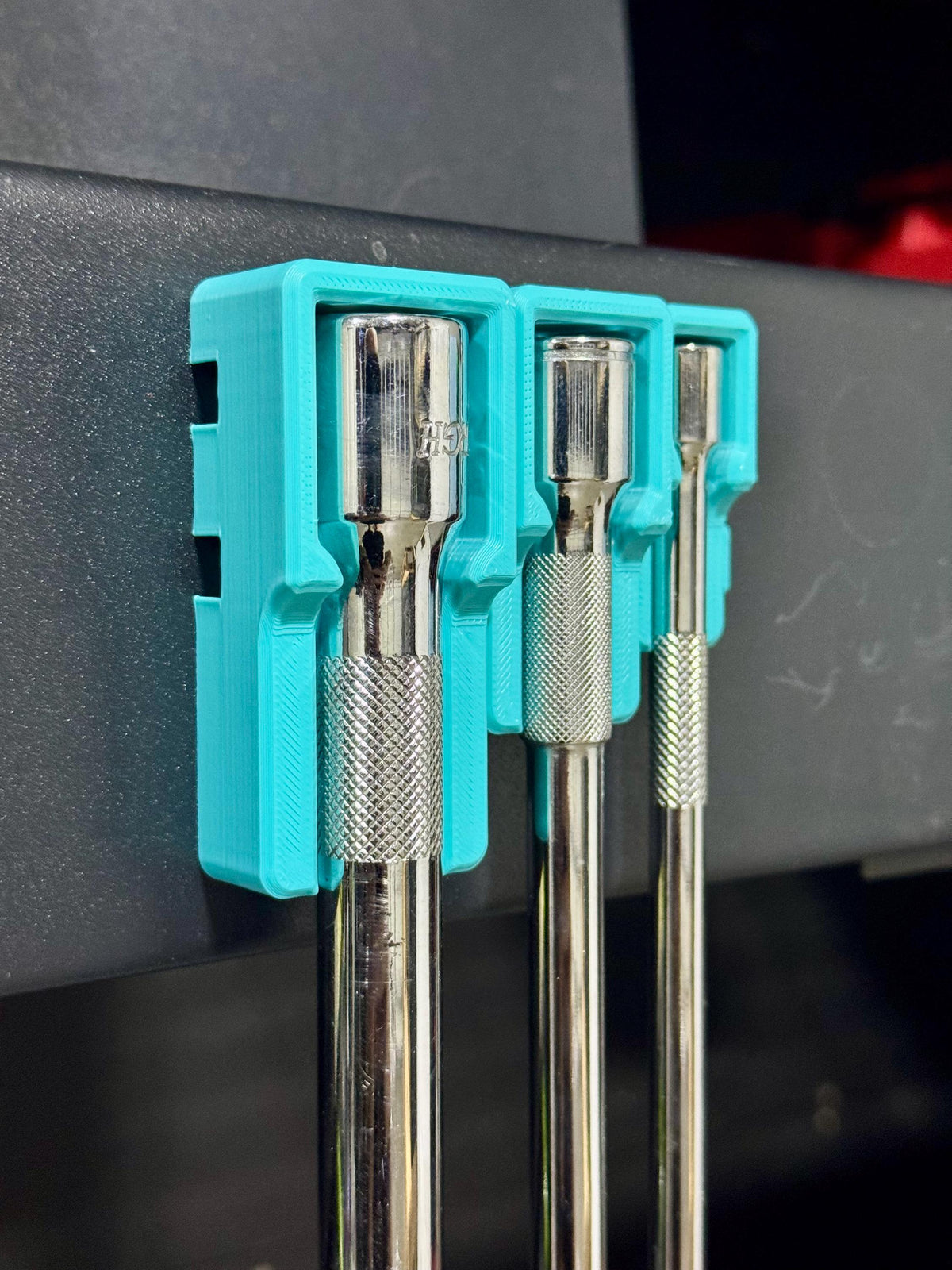 Side-angled view of teal holders supporting three hanging socket extensions on a tool cart.