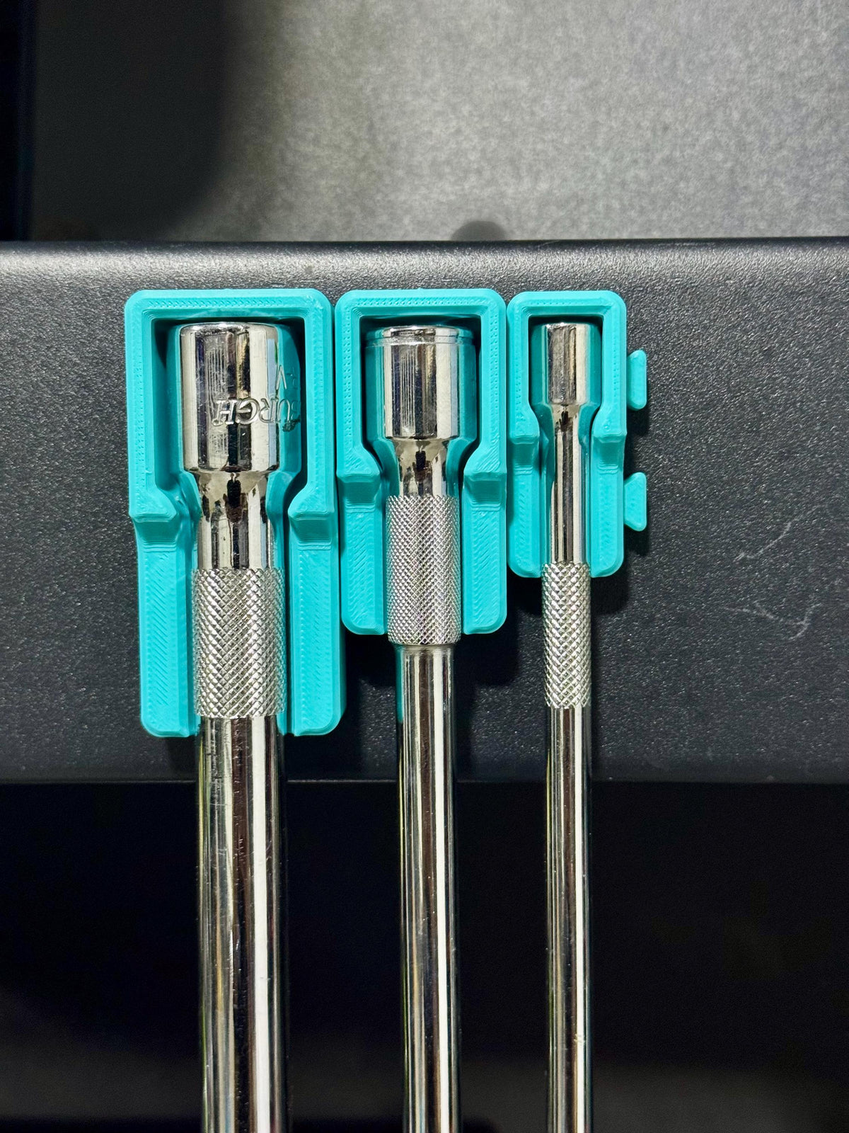 Front view of three socket extensions hanging from teal holders attached to a dark tool-cart side.