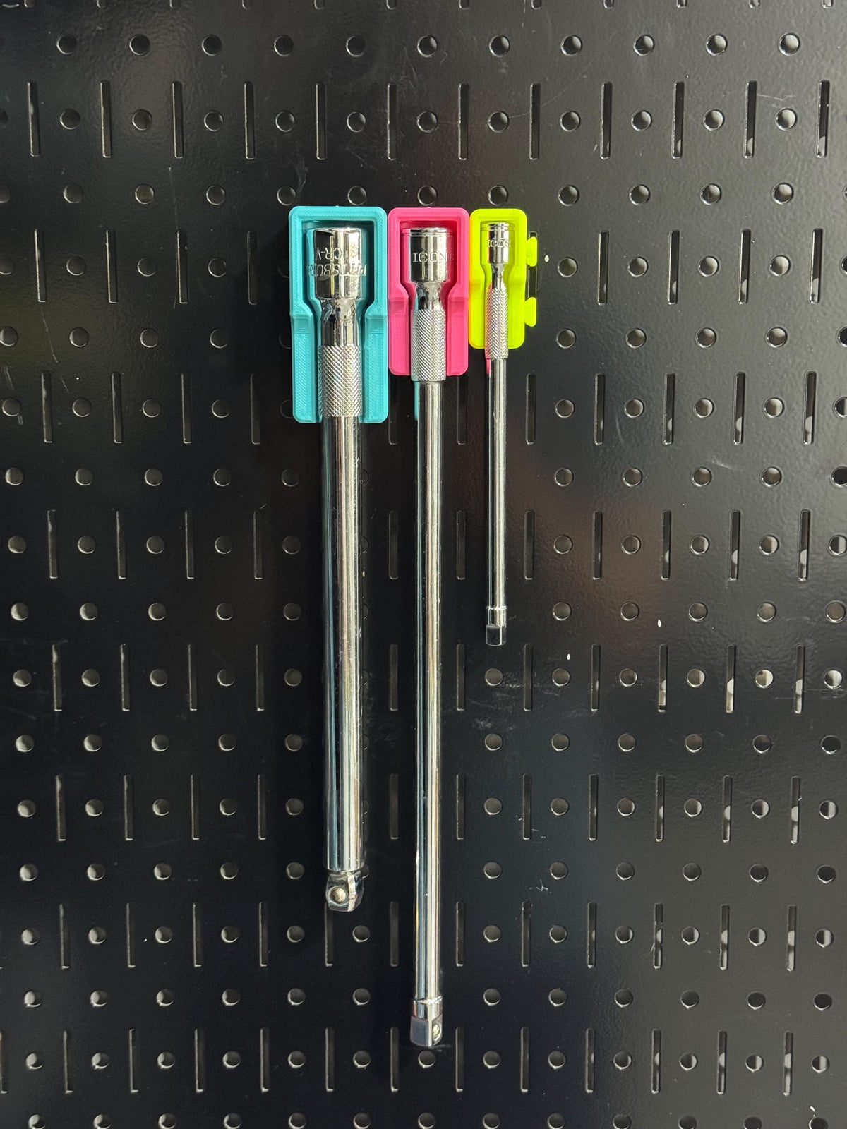 Wide view of three socket extensions stored upright against a black pegboard in colorful holders.