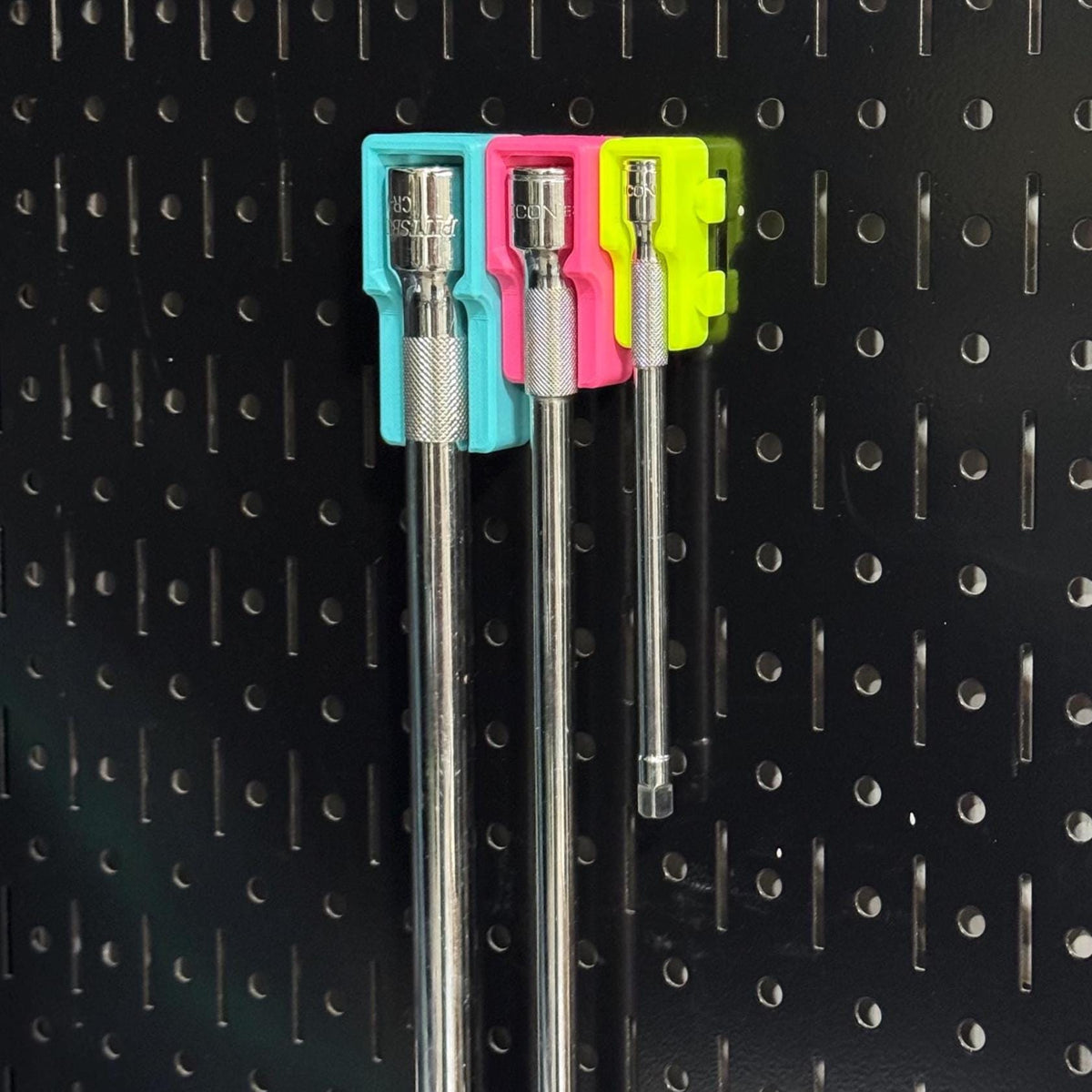 Angled view of three hanging extension bars in teal, pink and yellow pegboard-mounted holders.