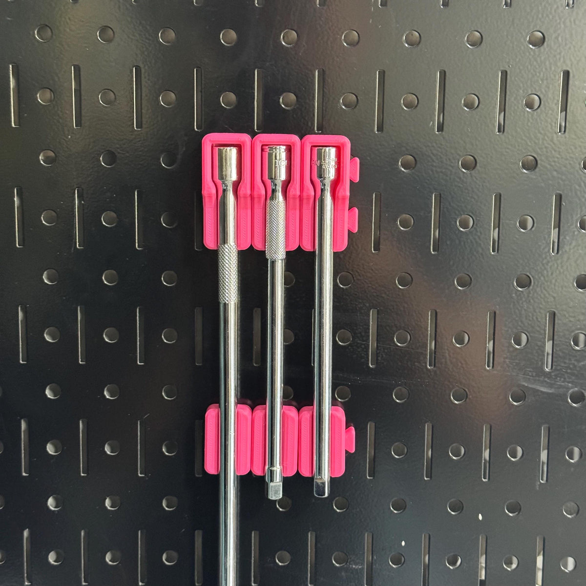 Three extensions held on black pegboard by pink head holders and pink lower support blocks.