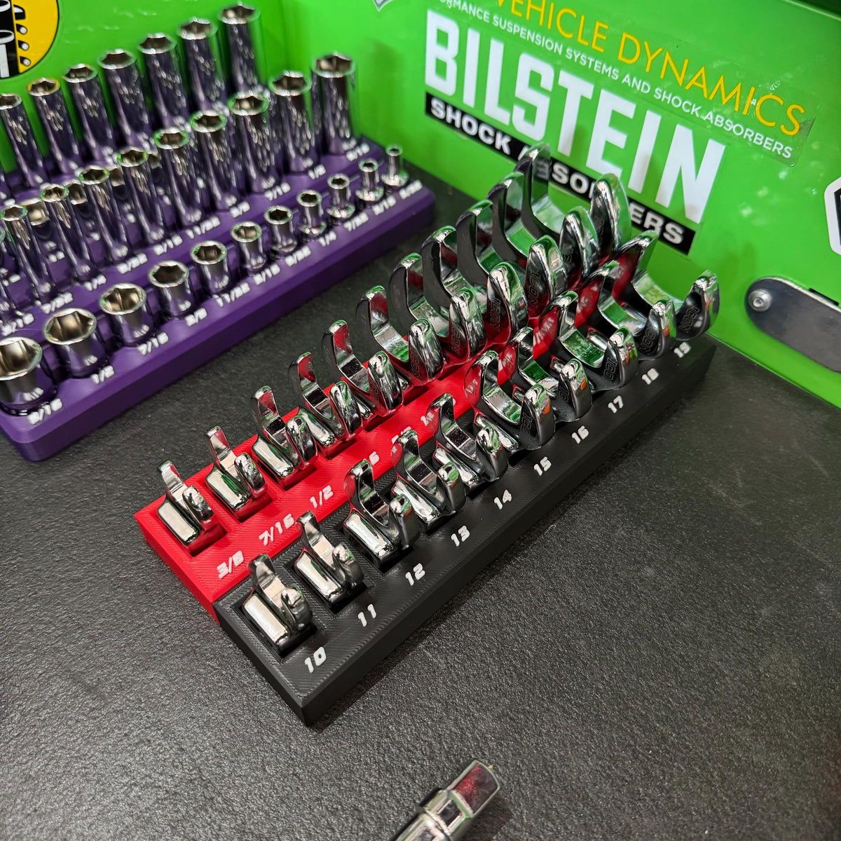 Crowfoot wrenches in red and black holders with white size labels inside a toolbox.