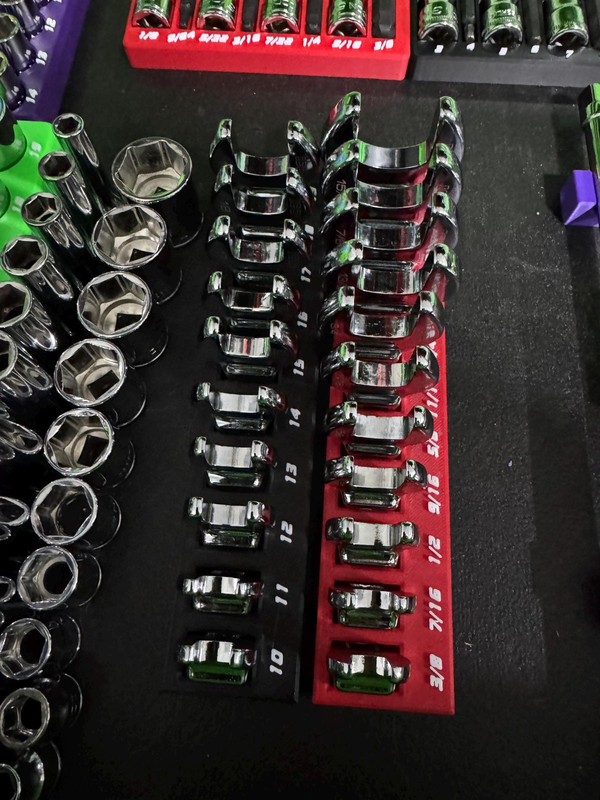 Red and black crowfoot wrench holders positioned between socket rows and extension bars in a toolbox.