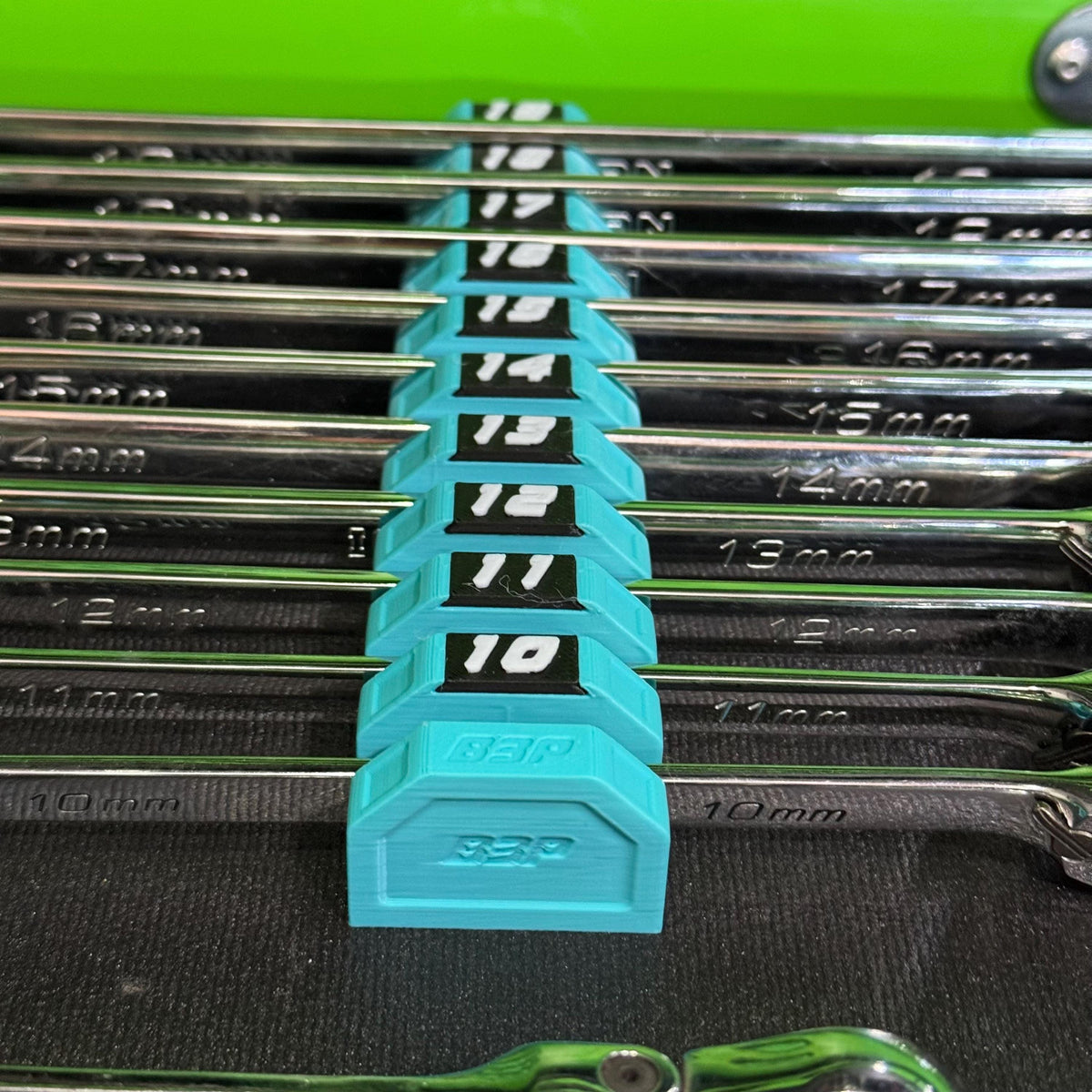 Close-up of a teal end cap and numbered modular holders supporting chrome wrenches.