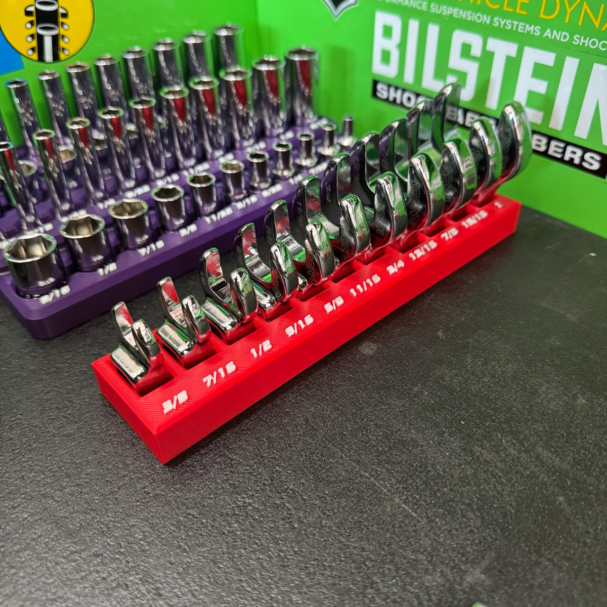 Low angled view of crowfoot wrenches standing in a red size-labeled holder beside a purple socket tray.