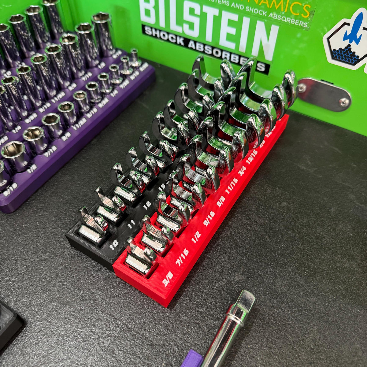 Angled view of crowfoot wrenches arranged by size in red and black labeled holders beside socket trays.