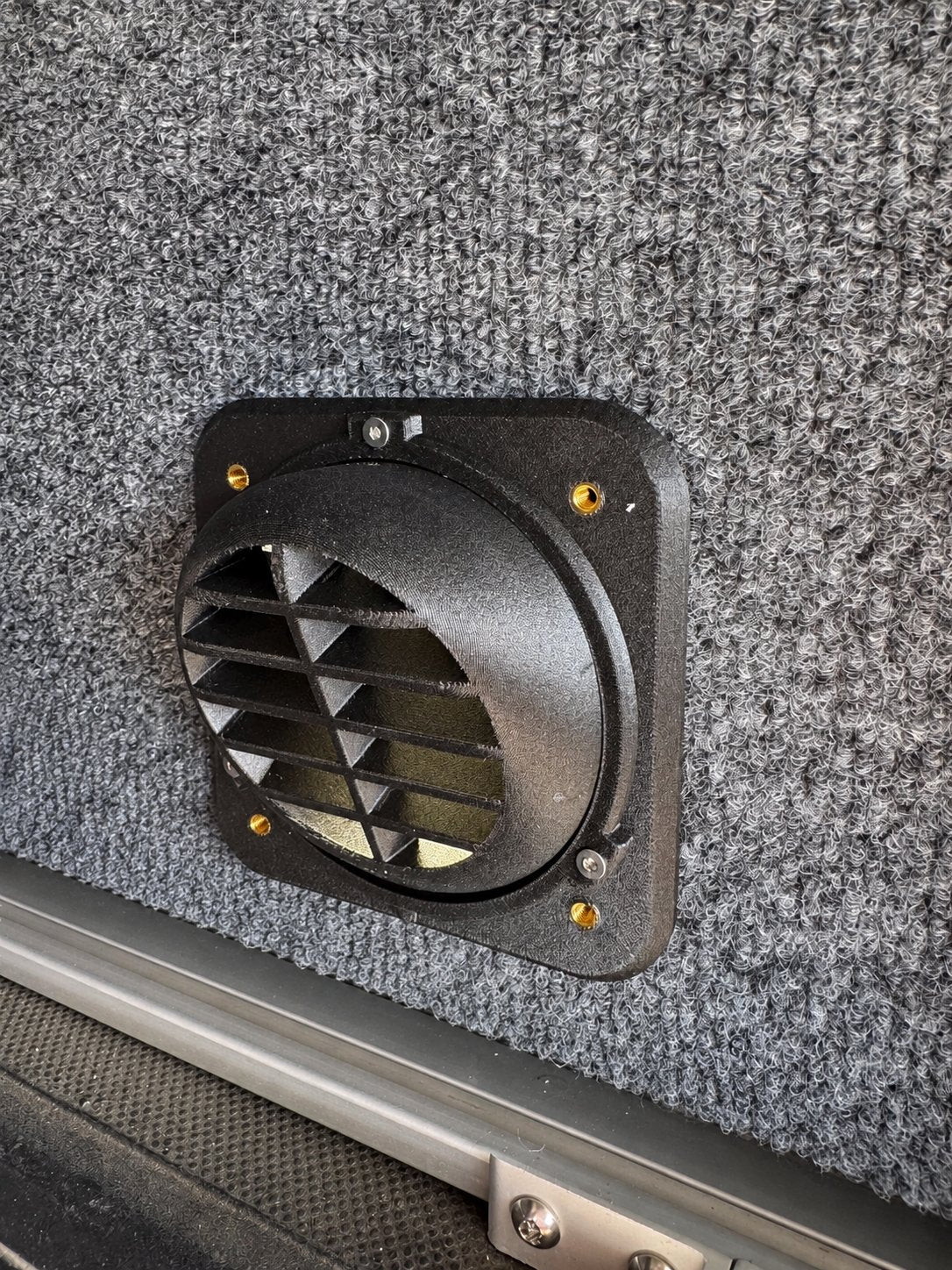 Black directional heater vent mounted inside a carpet-lined camper wall.