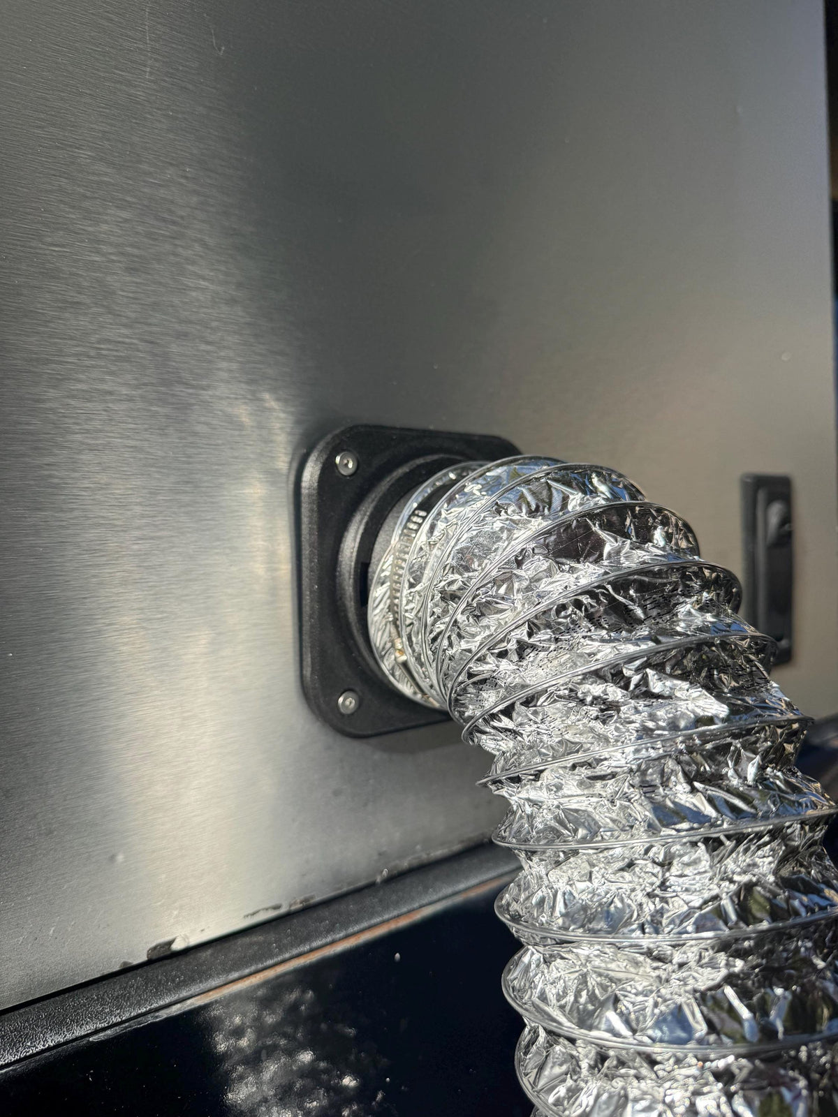 Silver flexible heater duct attached to the camper wall port and curving downward.