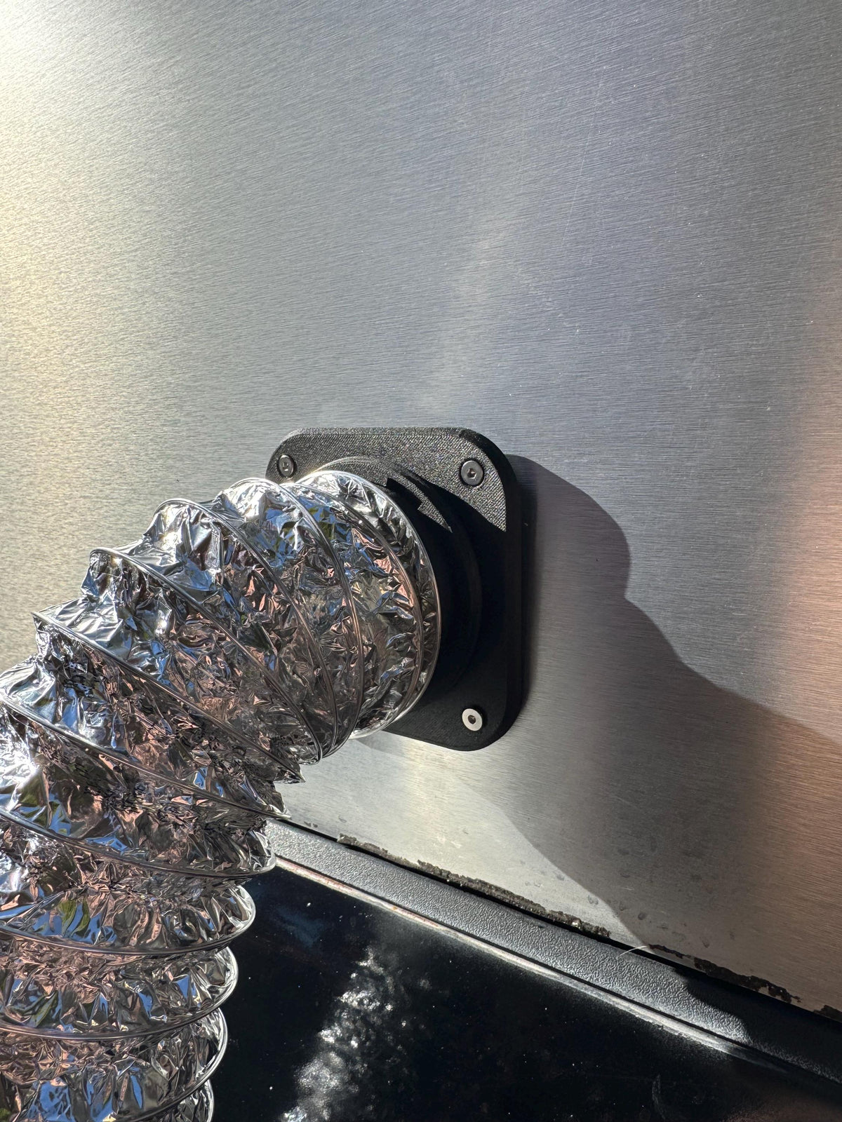 Flexible silver heater duct connected to a black camper wall port, viewed from below.