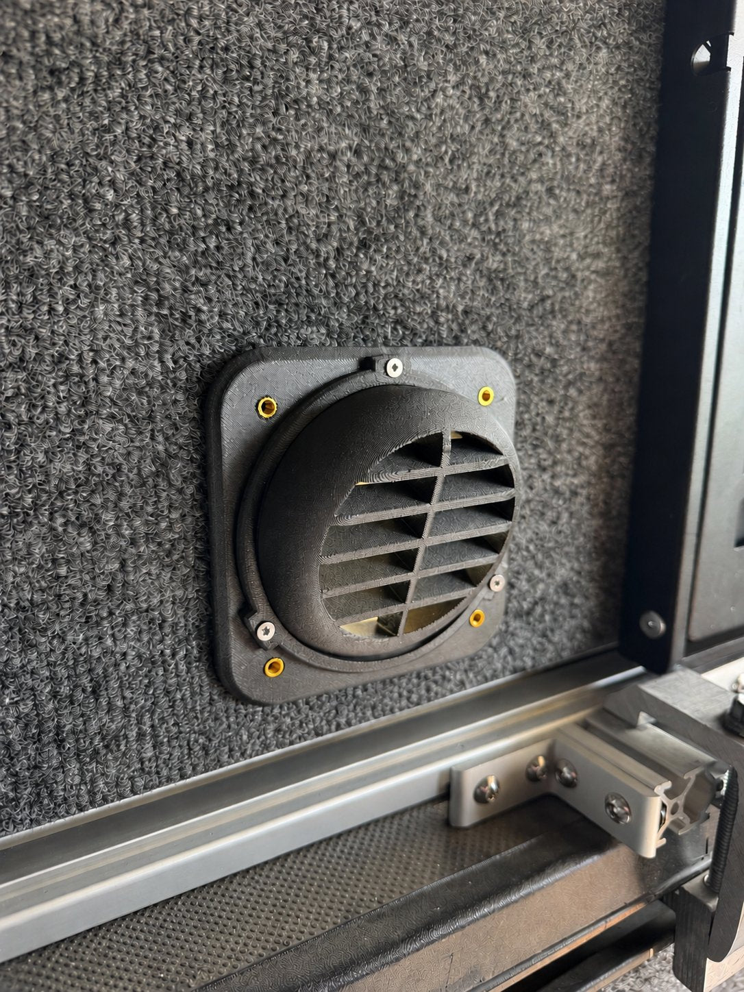 Angled view of a black directional heater vent on a carpet-lined camper wall.