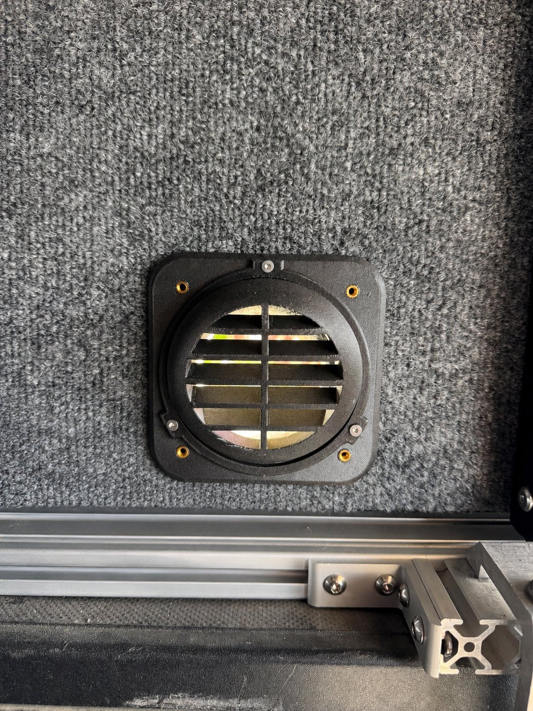 Front view of a black louvered heater vent above a camper interior rail.
