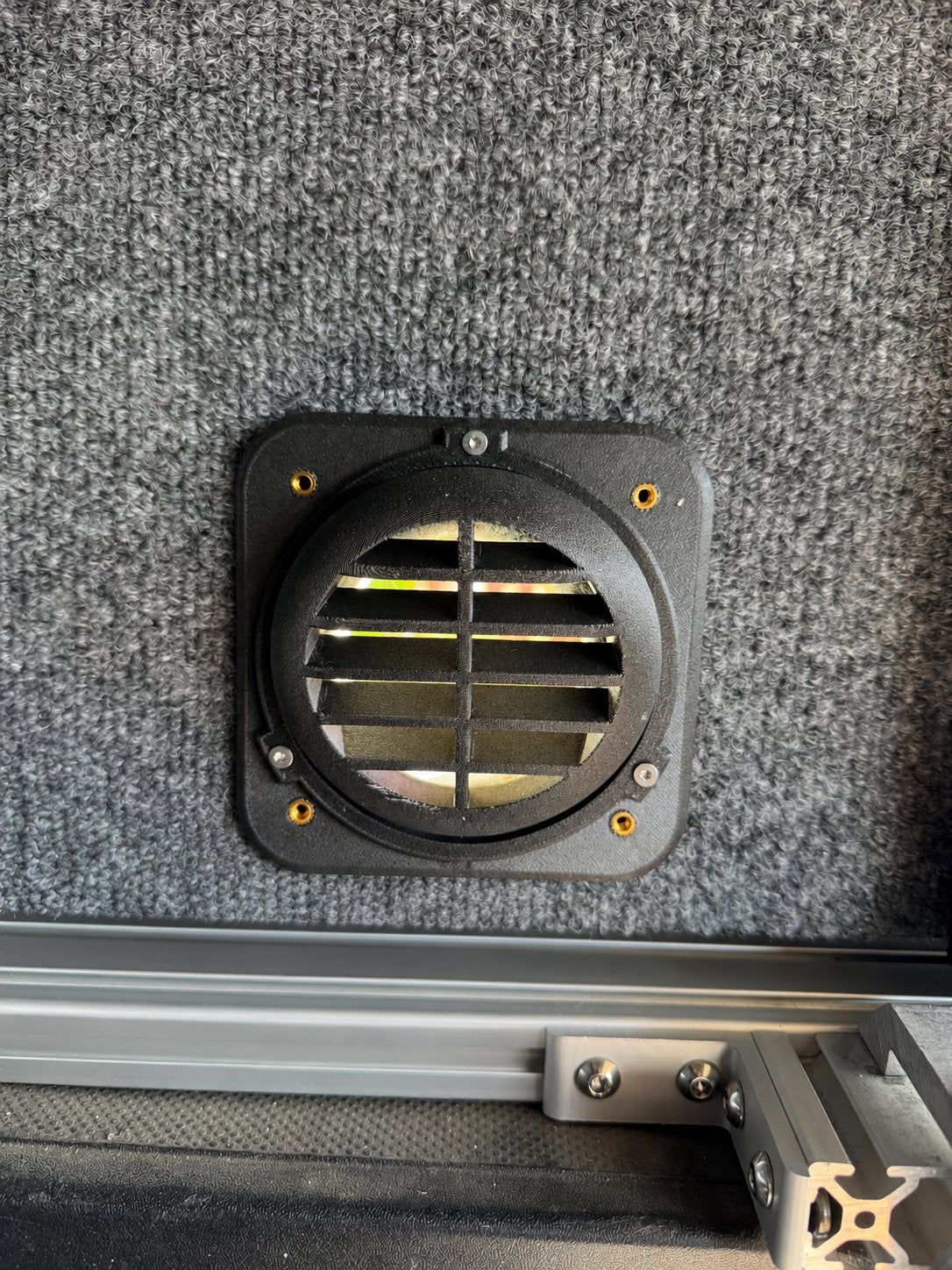 Black louvered heater vent installed on a carpet-lined wall above camper hardware.